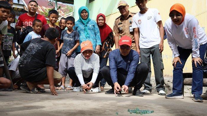 Wali Kota Makassar Danny Pomanto didampingi Indira Yusuf Ismail ikut bermain kelereng bersama anak Pulau Barrang Lompo, Jumat (12/7/2024). 
 