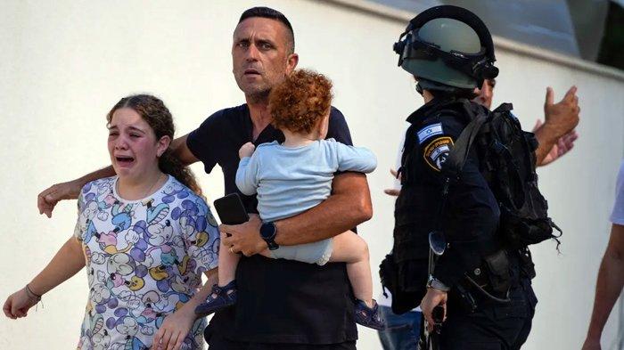 Petugas polisi Israel mengevakuasi sebuah keluarga dari lokasi yang terkena roket di Ashkelon. (Tsafrir Abayov/AP via Aljazeera)