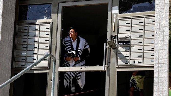 Seorang pria yang mengenakan selendang Yahudi Israel melihat keluar dari pintu masuk sebuah gedung yang rusak. (Ammar Awad/Reuters via Aljazeera)