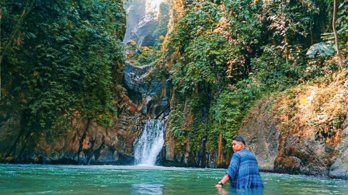 SEORANG pengunjung berfoto denganlatar belakang air terjun Sampuren Putih, Kamis (26/3/2020).