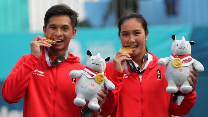 Atlet tenis ganda campuran Indonesia, pasangan Christopher Benjamin Rungkat/Aldila Sutjiadi menggigit medali emas yang berhasil mereka raih usai mengalahkan pasangan Thailand, Sonchat Ratiwatana/Luksika Kumkhum pada ajang Asian Games 2018 di Jakabaring Sport City, Palembang, Sumatera Selatan, Sabtu (25/8/2018). (Tribun Sumsel/Abriansyah Liberto)