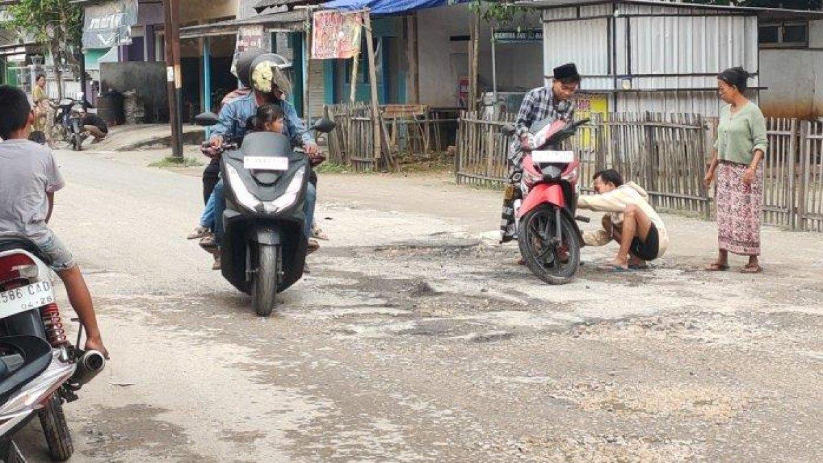 100 HARI KERJA - Dua remaja menjadi perhatian warga setelah motor Honda Supra terjatuh karena terjerembab lubang jalan saat melintasi Jalan Raya Pasar Jaddih, Desa Jaddih, Kecamatan Socah, Minggu (9/3/2025). Kebijakan efisiensi anggaran oleh Presiden RI Prabowo Subianto membayangi program prioritas Bupati Bangkalan, Lukman Hakim, yakni jalan kabupaten tanpa lubang.