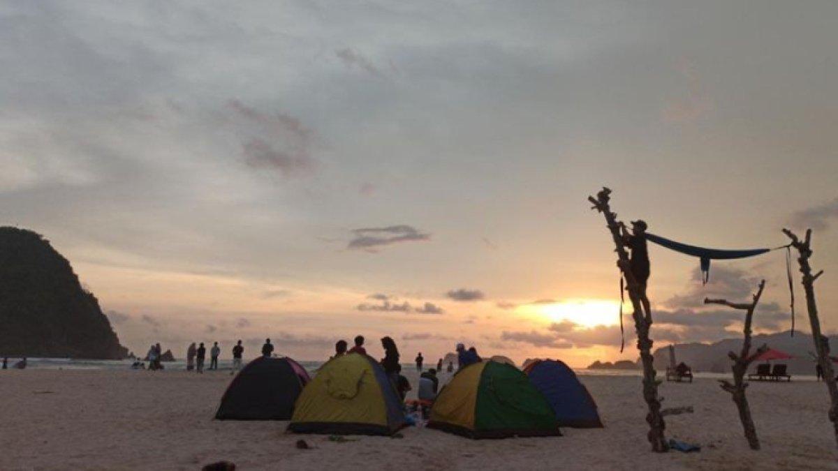 WISATA AIR - Potret wisatawan menggelar camping di Pantai Pulau Merah, disadur dari Kompas.com pada Rabu (12/3/2025). Pantai Pulau Merah tawarkan panorama sunset yang menarik.