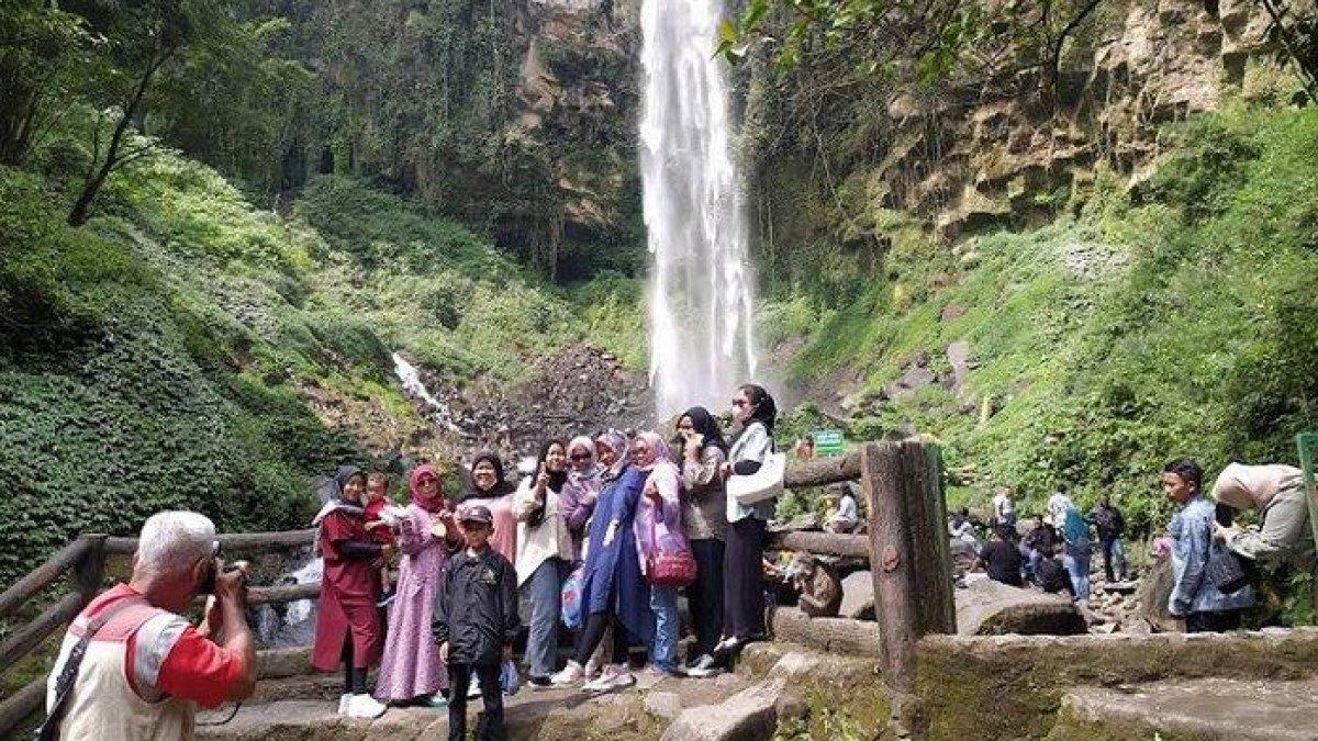 WISATA AIR TERJUN - Penyedia jasa foto, Hendro saat memotret rombongan wisata di kawasan Air Terjun Grojogan Sewu Tawangmangu Kabupaten Karanganyar, Sabtu (2/7/2022).