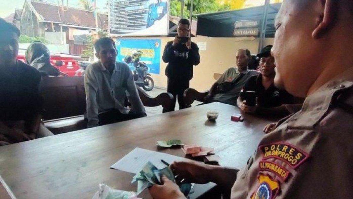Polisi menghitung uang temuan seorang pemuda saat melintas jalan simpang empat Kalurahan Pengasih, Kapanewon Pengasih, Kabupaten Kulon Progo, Daerah Istimewa Yogyakarta. Pemuda itu mencari pemilik uang dan berhasil mengembalikannya ke pemilik uang, difasilitasi polisi.