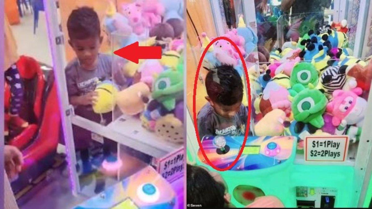 Seorang anak laki-laki menyelinap ke dalam mesin capit yang penuh dengan boneka mainan.