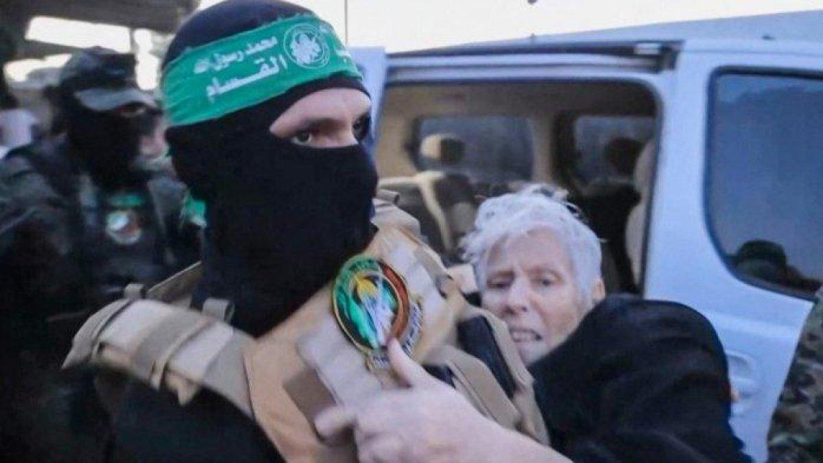 Gambar yang diambil dari video selebaran yang dirilis oleh Kantor Media Hamas menunjukkan seorang anggota Brigade Al-Qassam memimpin seorang sandera (kanan) ke pejabat Komite Palang Merah Internasional di Gaza pada 24 November 2023, di depannya dipindahkan ke Israel.