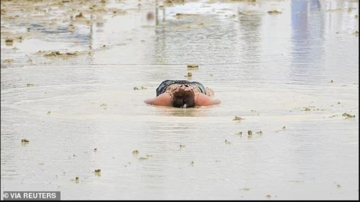 Seorang peserta Burning Man berbaring di lumpur dan air di acara tersebut