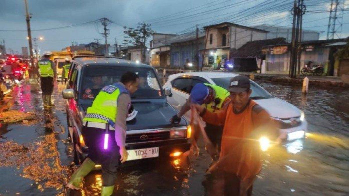 BANJIR DI DEMAK - Seorang petugas memasang tali derek satu unit mobil alami mogok di tengah banjir rob Pantura Semarang-Demak pada Minggu (6/4/2025) malam.
