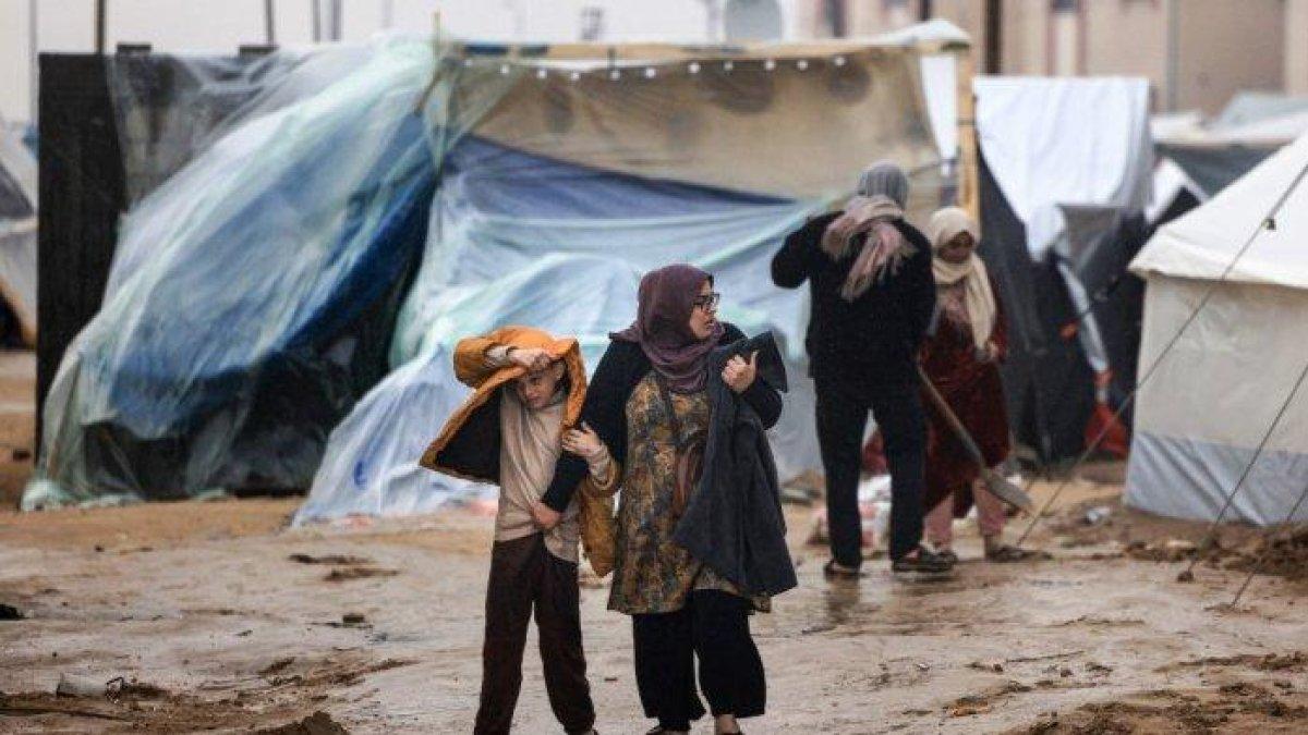 Warga Palestina berjalan di bawah hujan di sebuah kamp pengungsi di Rafah, di Jalur Gaza selatan tempat sebagian besar warga sipil mengungsi, pada 13 Desember 2023.