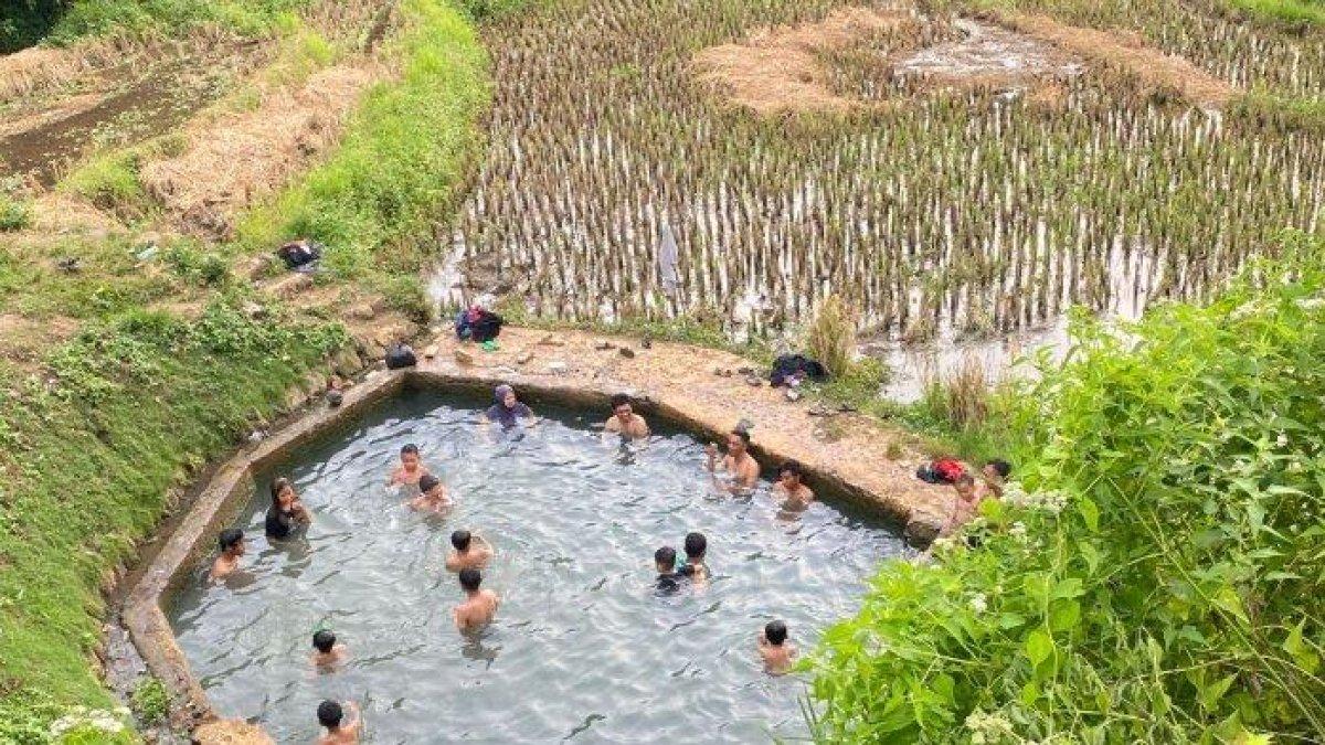 Tampak sejumlah anak bermain menikmati pemandian air panas di tengah hamparan sawah.