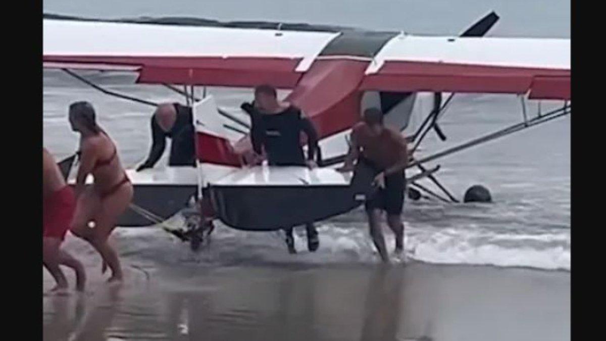 Pengunjung pantai membantu menarik pesawat kecil keluar dari air