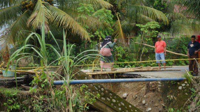 Seorang warga melintasi jembatan putus di korong dulu Ulakan Tapakis Padang Pariaman dengan meniti sejumlah susunan batang bambu 