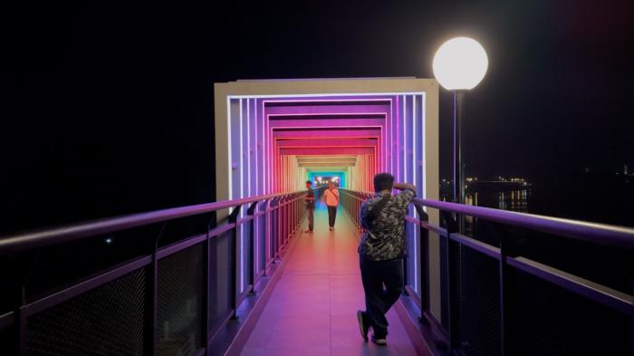 SKYWALK - Sejumlah wisatawan mengabadikan momen di titik lorong dancing light skywalk Tengku Buwang Asmara di malam hari, Rabu (30/7/2025).