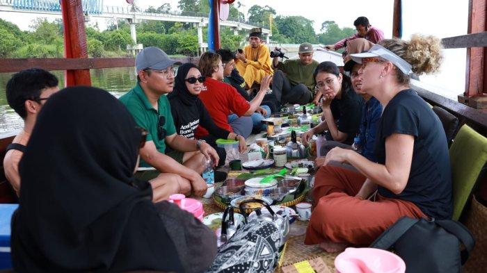 MAKAN BERHANYUT - Wisatawan asal Brazil dan Malaysia makan di atas perahu kayu di sungai Siak, Minggu (4/5/2025). Makan Berhanyut menjadi salah satu wisata unggulan di Kabupaten Siak.