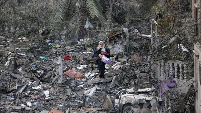 Seorang perempuan Palestina berjalan di atas puing-puing bangunan menyusul serangan Israel di Rafah, Jalur Gaza selatan pada Senin (20/11/2023).