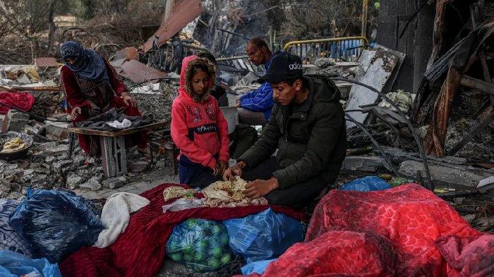 Warga Palestina makan di luar, dikelilingi kehancuran akibat serangan udara Israel di desa Khuzaa, sebelah timur Khan Younis di selatan Jalur Gaza pada 27 November 2023.