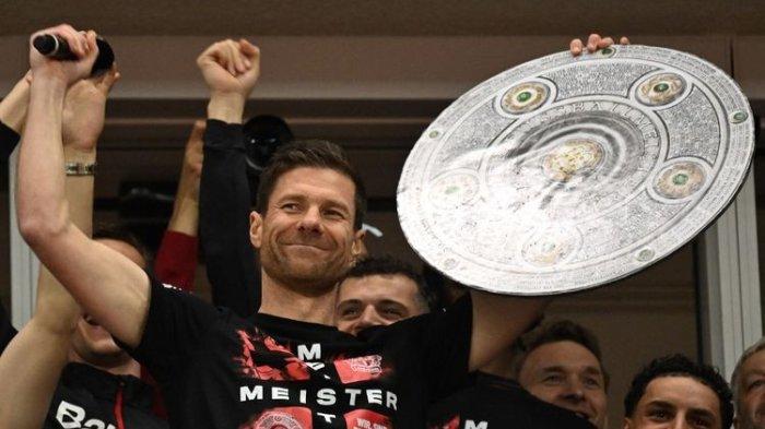 Bayer Leverkusen membungkus gelar juara Bundesliga 2023-2024 dengan pesta gol 5-0 ke gawang Werder Bremen pada Minggu (14/4/2024). Pelatih Xabi Alonso berpose dengan trofi juara Liga Jerman usai laga tersebut.