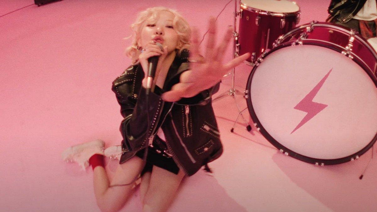 Rose BLACKPINK mengenakan crop top putih, skort kulit, dan jaket kulit di MV Lagu Terbaru 'APT'.