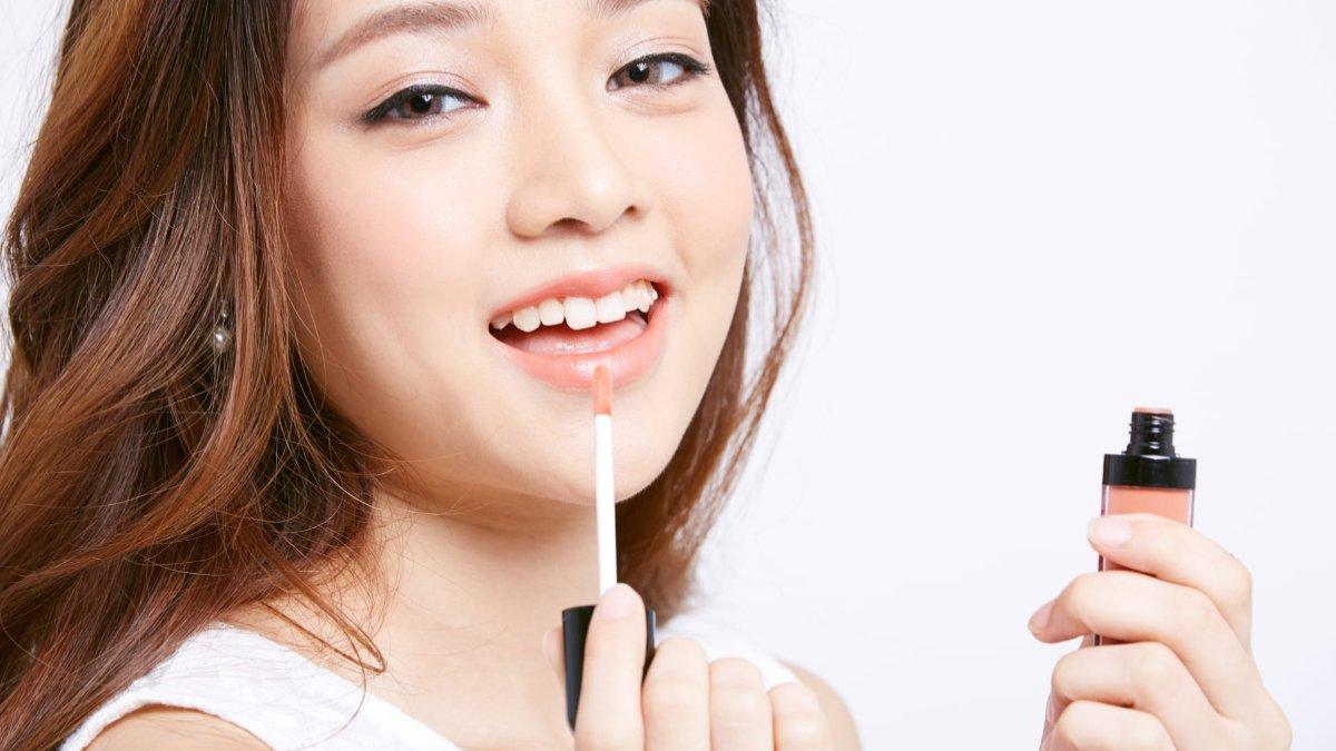 Ilustrasi wanita menggunakan lip gloss dengan warna sheer.