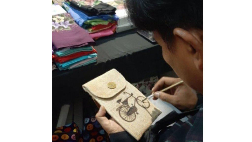 Seorang pegawai nasrafa sedang melukis sepeda di pouch untuk Handphone (HP).