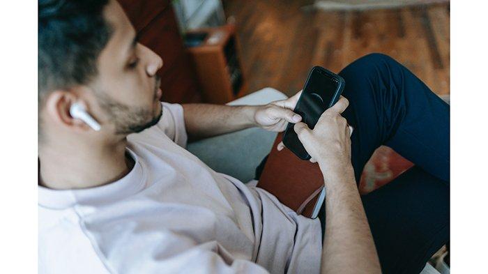 Ilustrasi seorang memasangkan earphone wireless atau TWS ke HP
