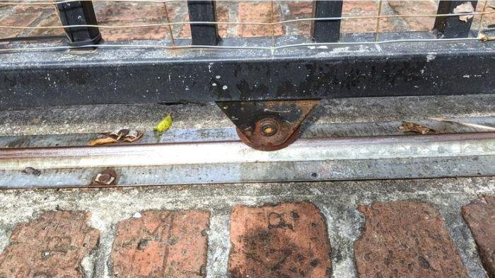 Ilustrasi sampah daun yang mengotori area di sekitar rel dan roda pintu pagar