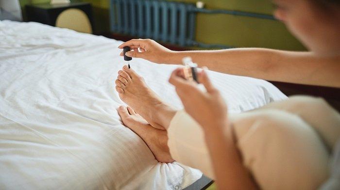 Ilustrasi wanita mengaplikasikan nail polish pada kuku kaki.