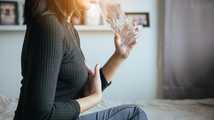 Ilustrasi minum air putih hangat untuk meredakan nyeri perut saat haid.