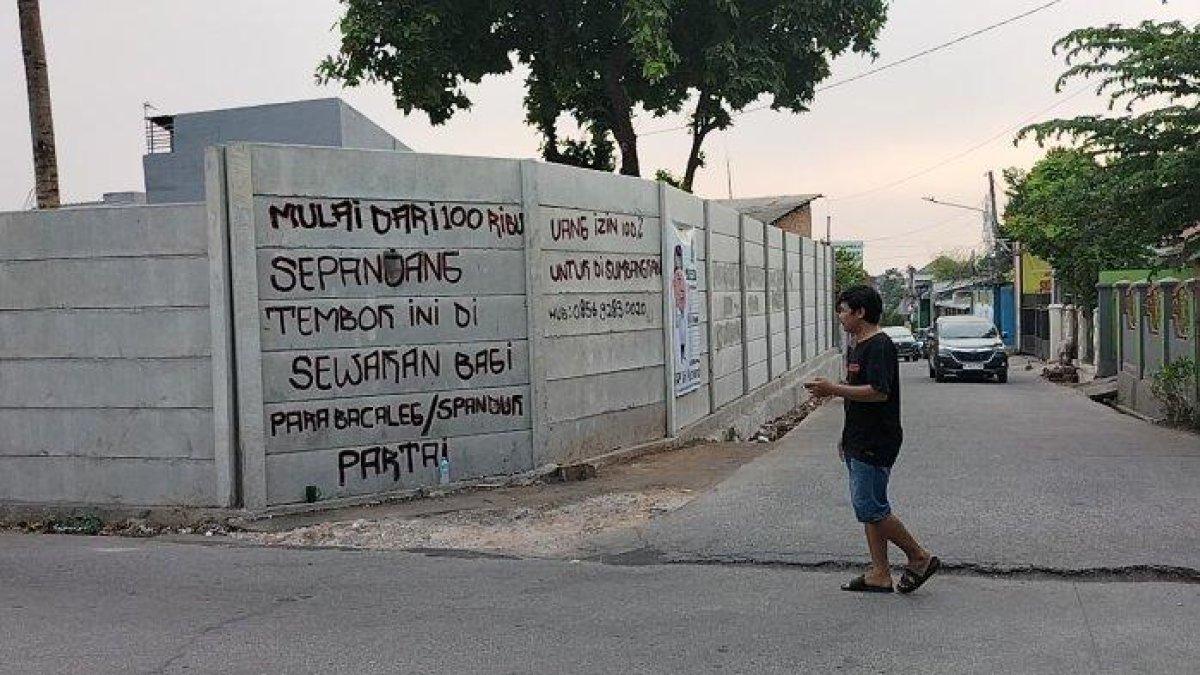 Tulisan atau coretan tembok berisi pengumuman tarif Rp100 ribu pemasangan spanduk caleg dan parpol di Jalan Raya Kampung Setu, Bekasi Barat, Kota Bekasi, Rabu (11/10/2023)