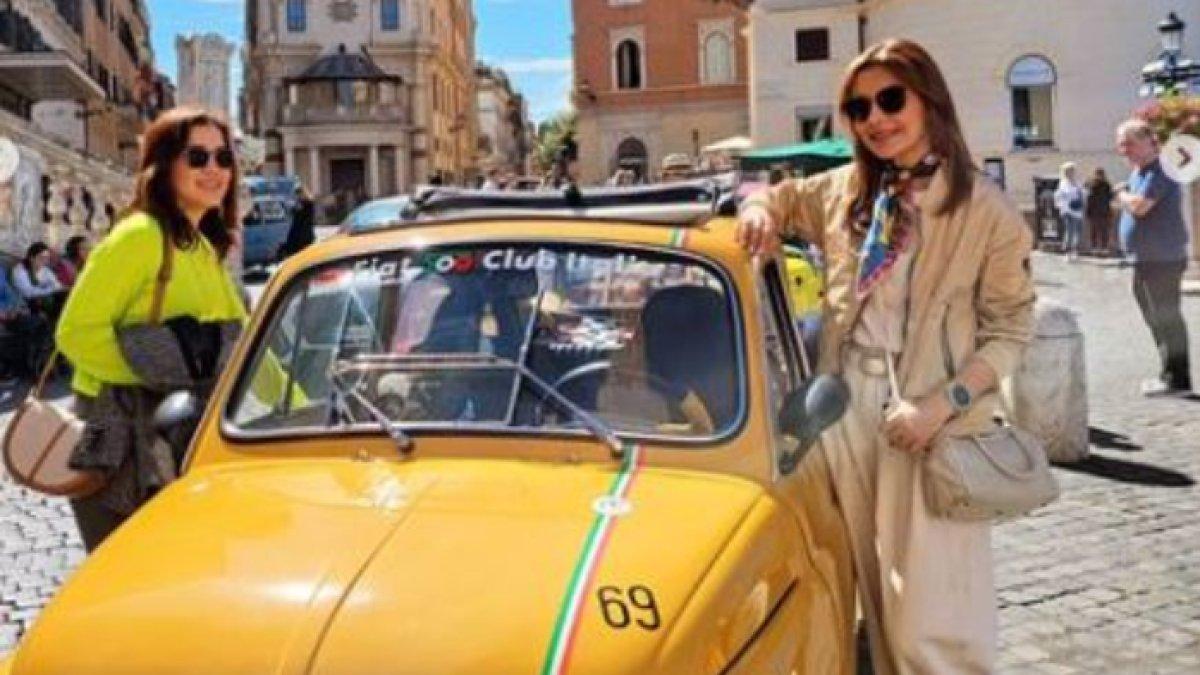 Foto Najwa Shihab eksis berpose dengan mobil kuning menyala dipayungi cakrawala biru.