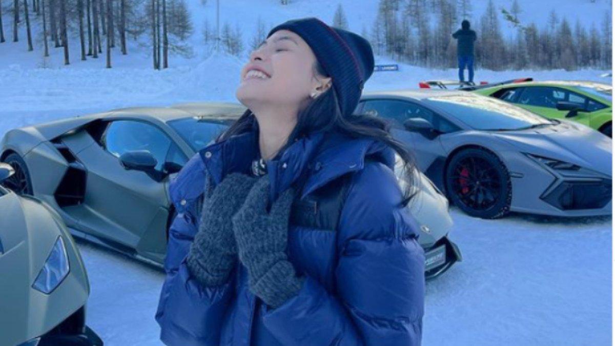 Maudy berfoto dengan background sejumlah mobil yang berjejer.