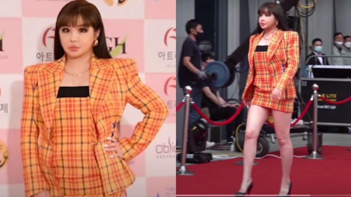 Park Bom mengenakan setelan jas motif kotak-kotak berwarna oranye.