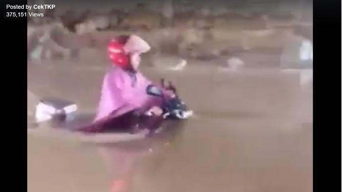 Seorang ibu mengendarai motor di tengah banjir.