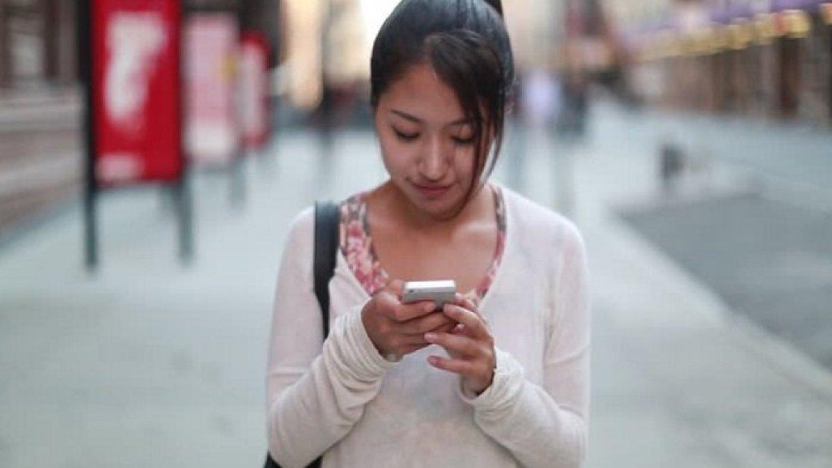 Wanita sedang berseri-seri saat membaca pesan di ponselnya