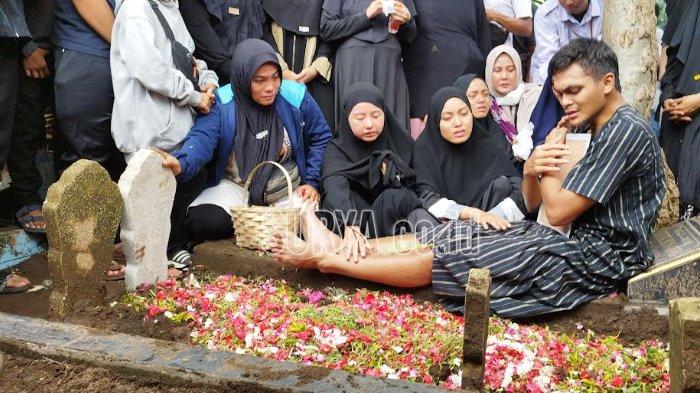 DUKA MENDALAM - Rachmat Irianto (Rian), duduk di samping pusara ayahnya Bejo Sugiantoro di TPU Geluran memeluk erat foto mendiang ayahnya setelah selesai proses pemakaman di TPU Geluran, Sidoarjo, Rabu (26/2/2025).