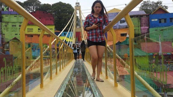 Sejumlah wisatawan saat melintas di jembatan kaca kampung Warna Warni Malang