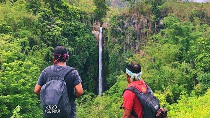Dua pengunjung melihat Air Terjun Murunderu dari atas sebelum turun melewati jalan menurun.
