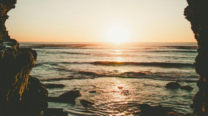 Ilustrasi pantai dengan pemandangan sunset yang terlihat di antara dua tebing.