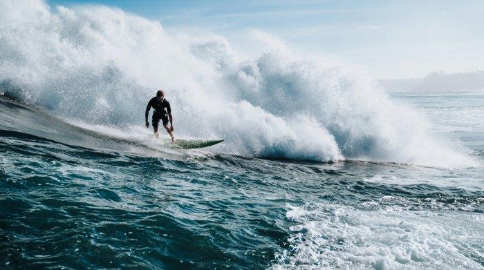 Ilustrasi wisatawan sedang berselancar atau surfing di pantai dengan ombak yang besar.