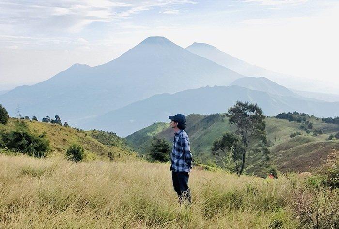 PUNCAK GUNUNG PRAU - Pendaki berfoto di puncak Gunung Prau dengan latar belakang Gunung Sindoro dan Gunung Sumbing yang menawan, Jumat (21/2/2025). Gunung Prau bisa menjadi pilihan untuk para pendaki pemuka. Cek itinerary dengan bujet Rp 190 ribuan berikut.