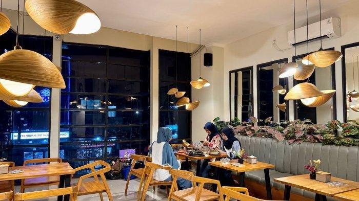 KULINER BOGOR - Pengunjung menikmati suasana malam di Gussanty Steak Grill Cafe. Interior kafe yang modern dengan sentuhan kayu dan pencahayaan hangat menciptakan suasana nyaman untuk bersantap.