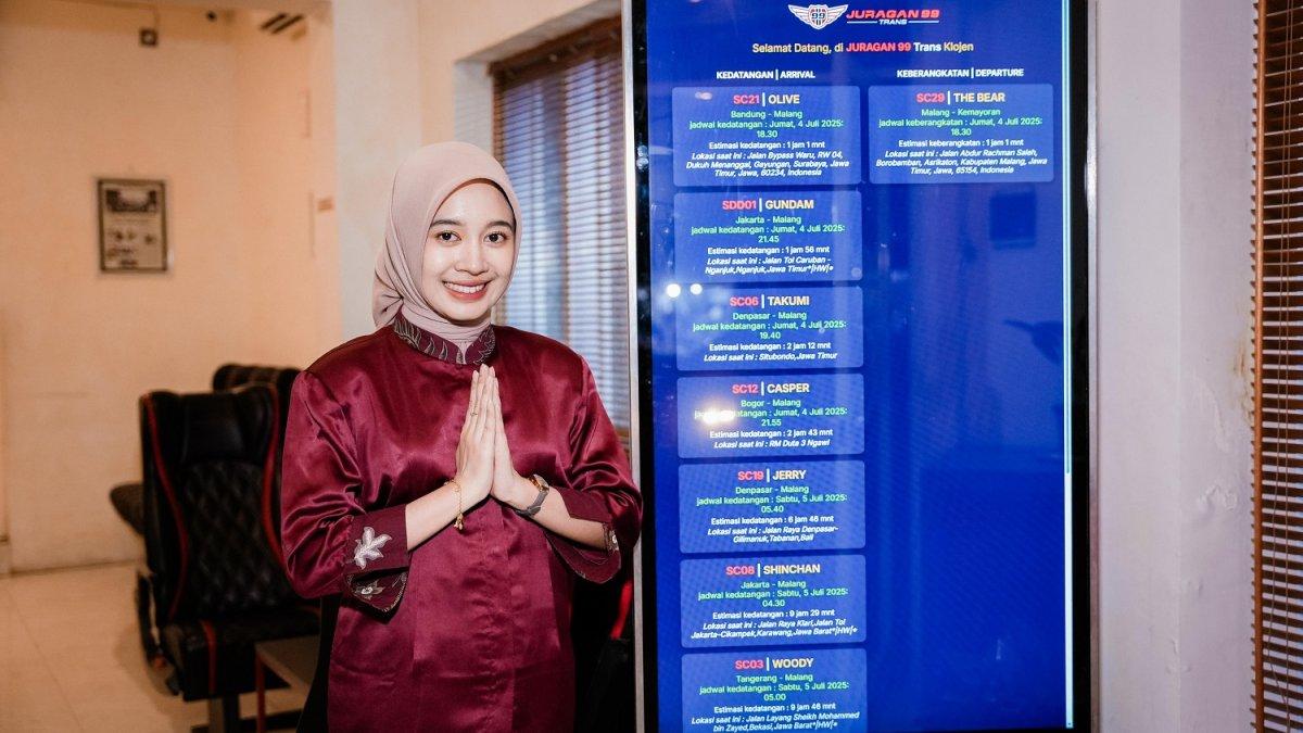 Petugas Juragan99 Trans di depan ETA Board yang menampilkan jadwal kedatangan dan keberangkatan bus secara real-time.