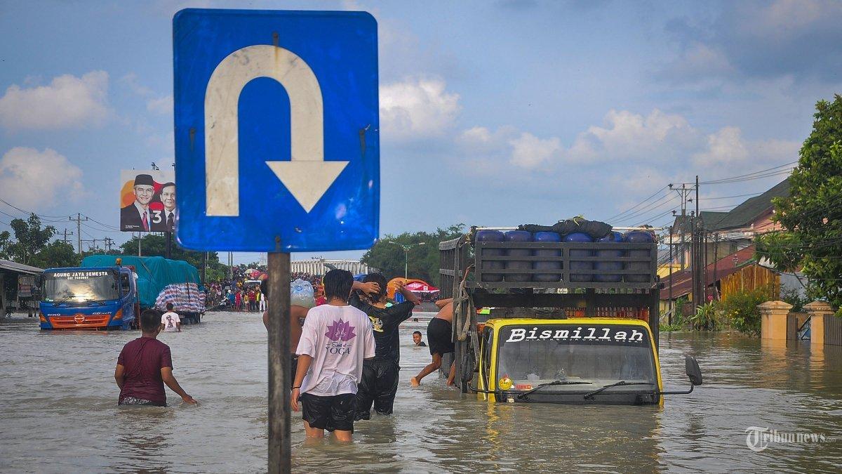 Masyarakat berjalan di jalan raya nasional yang terendam banjir akibat hujan deras dan jebolnya sungai di Demak, Jawa Tengah pada 11 Februari 2024.