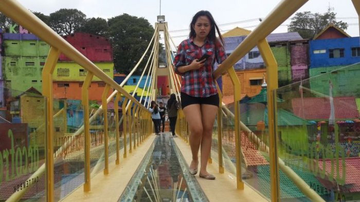 Sejumlah wisatawan saat melintas di jembatan kaca yang menghubungkan Kampung Warna-warni dan Kampung Tridi di Kota Malang, Jawa Timur, Selasa (10/10/2017).