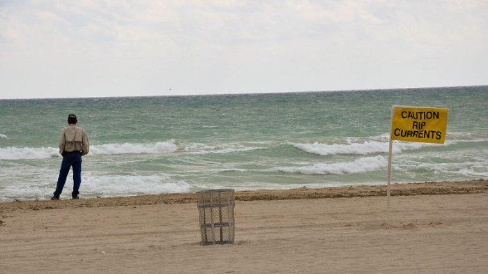 Seorang pria dan papan peringatan Rip current