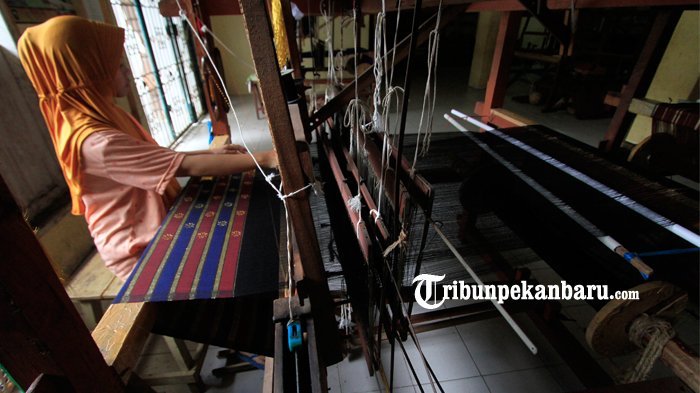 Seorang perajin songket sedang menenun kain songket.