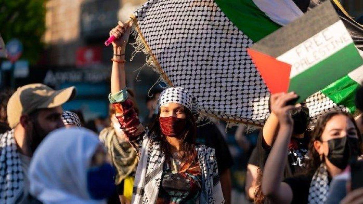 Foto Bella Hadid saat mengikuti demo Pro-Palestina di New York, Amerika Serikat, pada 14 Mei 2021. Ia mengenakan pakaian tradisional, Keffiyeh, masker wajah dan mengibarkan bendera besar Palestina.