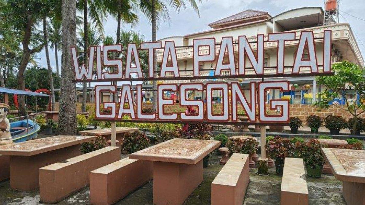 PANTAI GALESONG - Papan nama Wisata Pantai Galesong di Desa Sampulungan, Kecamatan Galesong Utara, Takalar, Sabtu (10/5/2025). Wisata Pantai Galesong sediakan berbagai fasilitas, dari wahana permainan jet sky, kolam renang, sampai aula kegiatan.