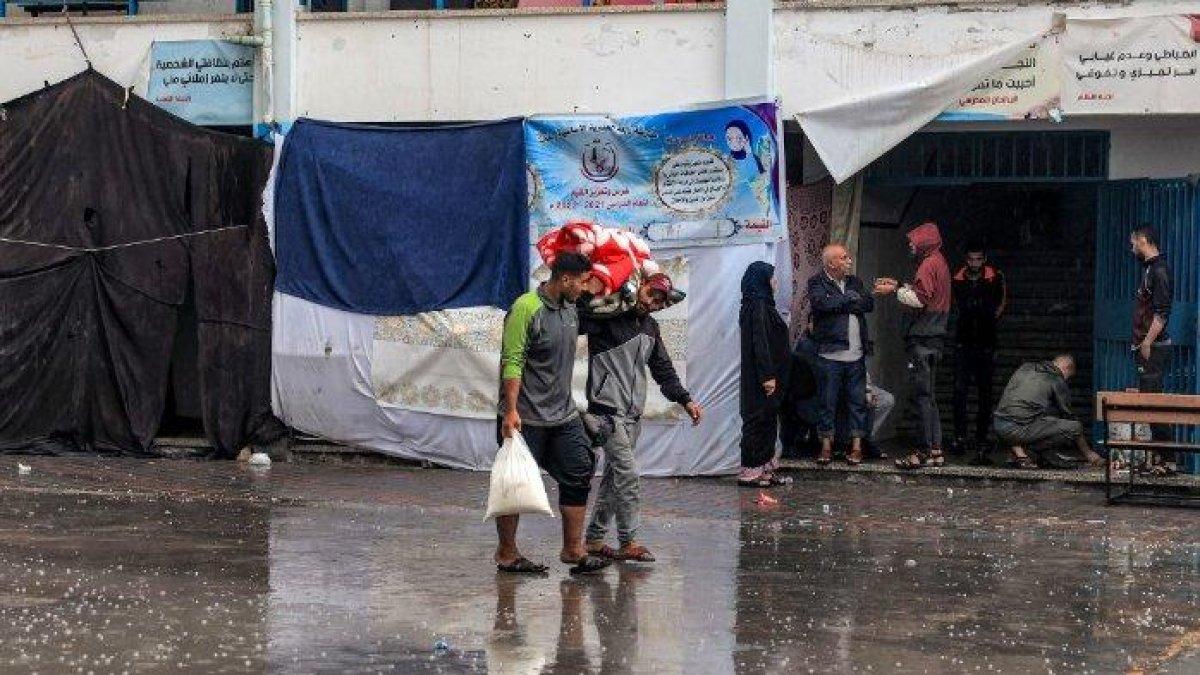 Para pria berjalan di tengah hujan sambil membawa selimut di halaman sekolah yang dikelola oleh Badan Bantuan dan Pekerjaan PBB untuk Pengungsi Palestina di Timur Dekat (UNRWA) di Rafah di Jalur Gaza selatan pada 14 November 2023